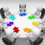 White humanoid figures sitting around a table with brightly coloured jigsaw puzzle pieces in front of them, indicating collaboration