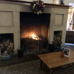 A warm fire in a large hearth with Christmas decorations above.