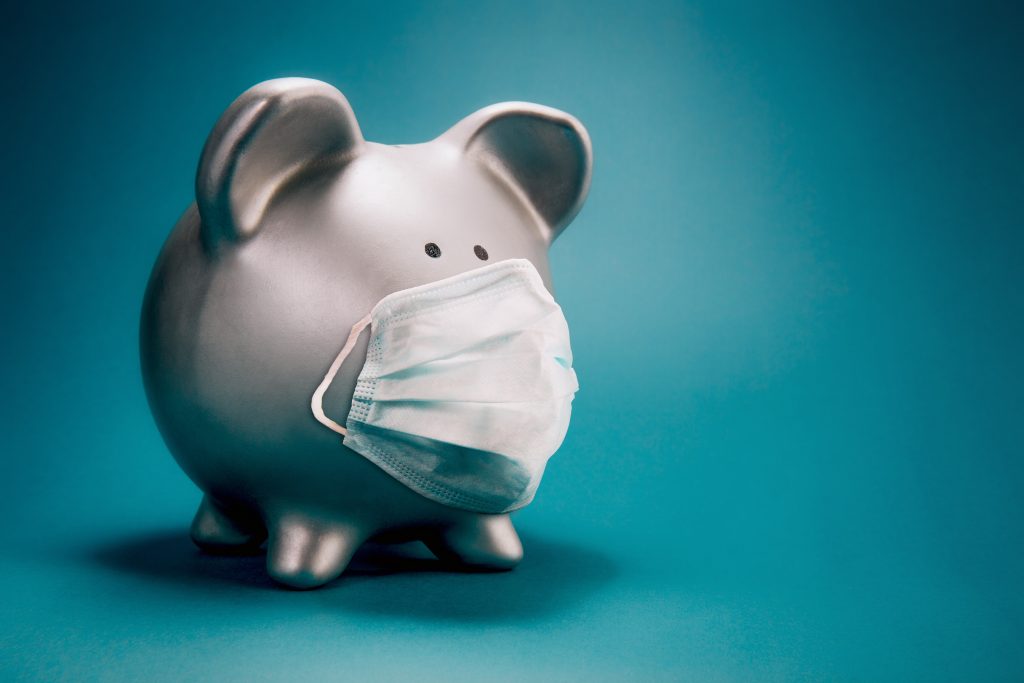 A grey piggy bank wearing a protective mask on a green background