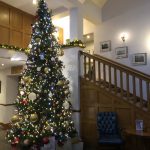 A large Christmas tree full of decorations at the Lancaster House Hotel. The staircase to the hotel's bedroom is next to the tree.