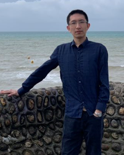 Yi Li standing by a wall with the sea behind him